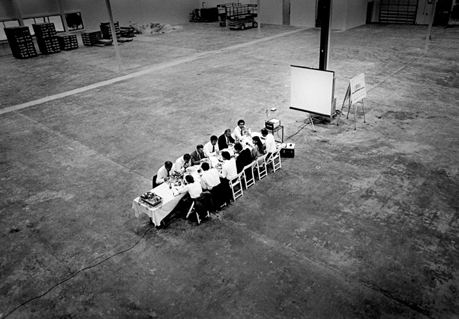 Executivos numa mesa dentro de um galpão - Foto de Doug Menuez