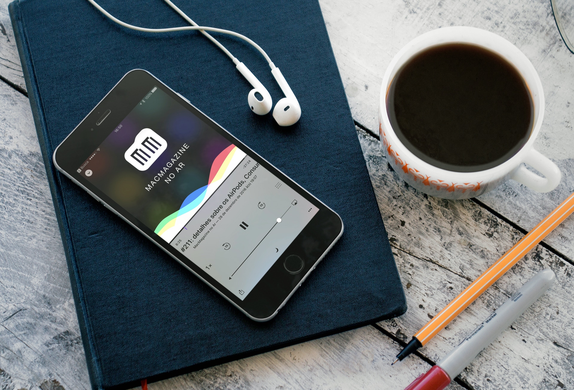Podcast #211 (MacMagazine no Ar) num iPhone sobre mesa com café e fones de ouvido