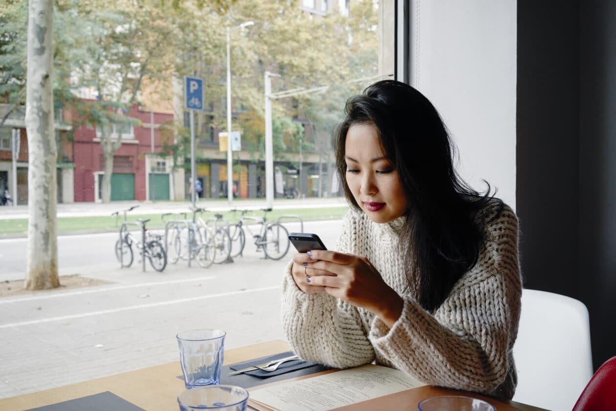 Mulher asiática mexendo em iPhone numa cafeteria