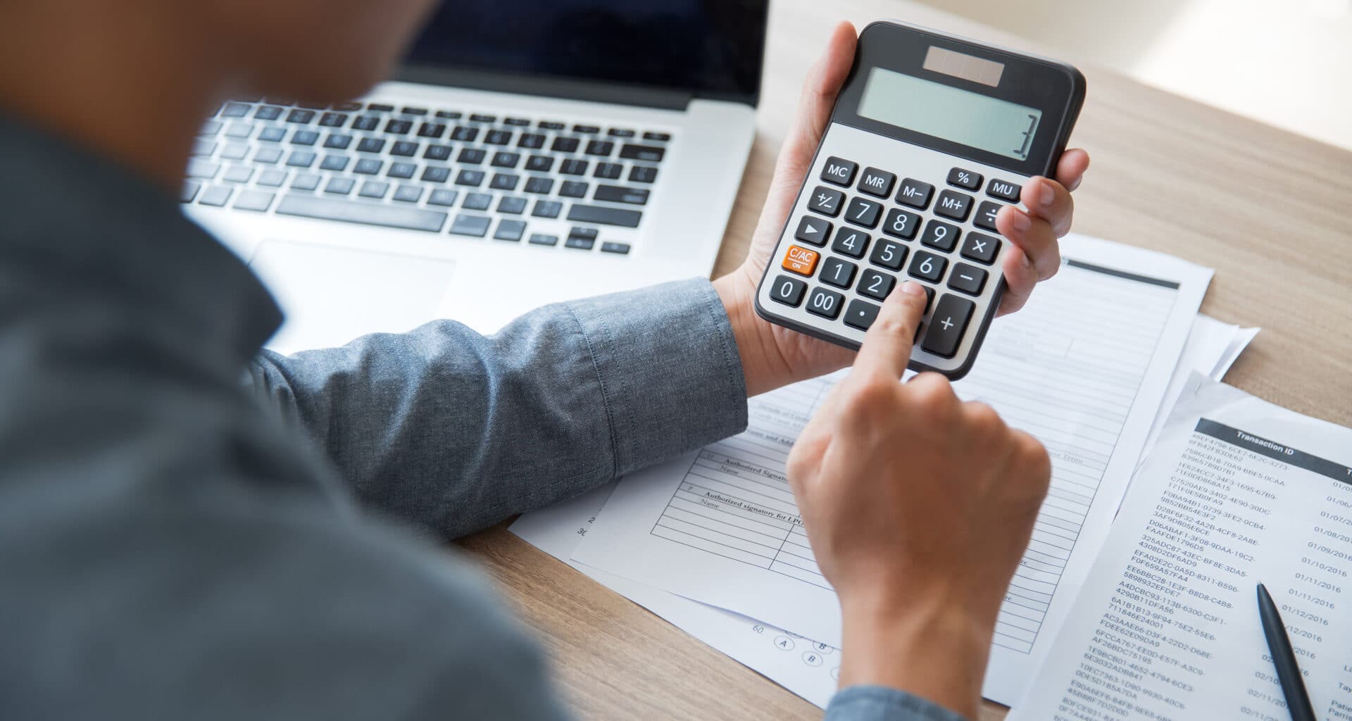 Pessoa usando uma calculadora com um Mac ao lado