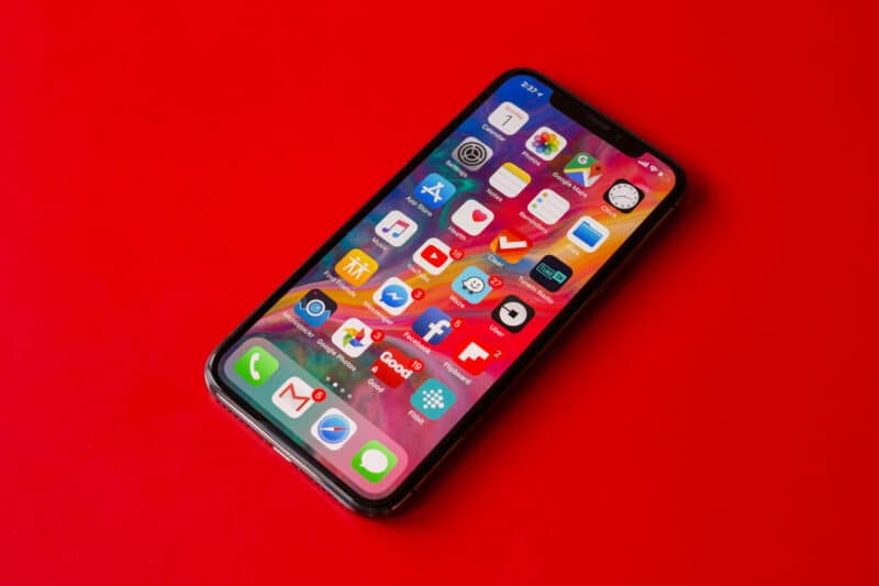 Tela de início de um iPhone com apps sobre mesa vermelha
