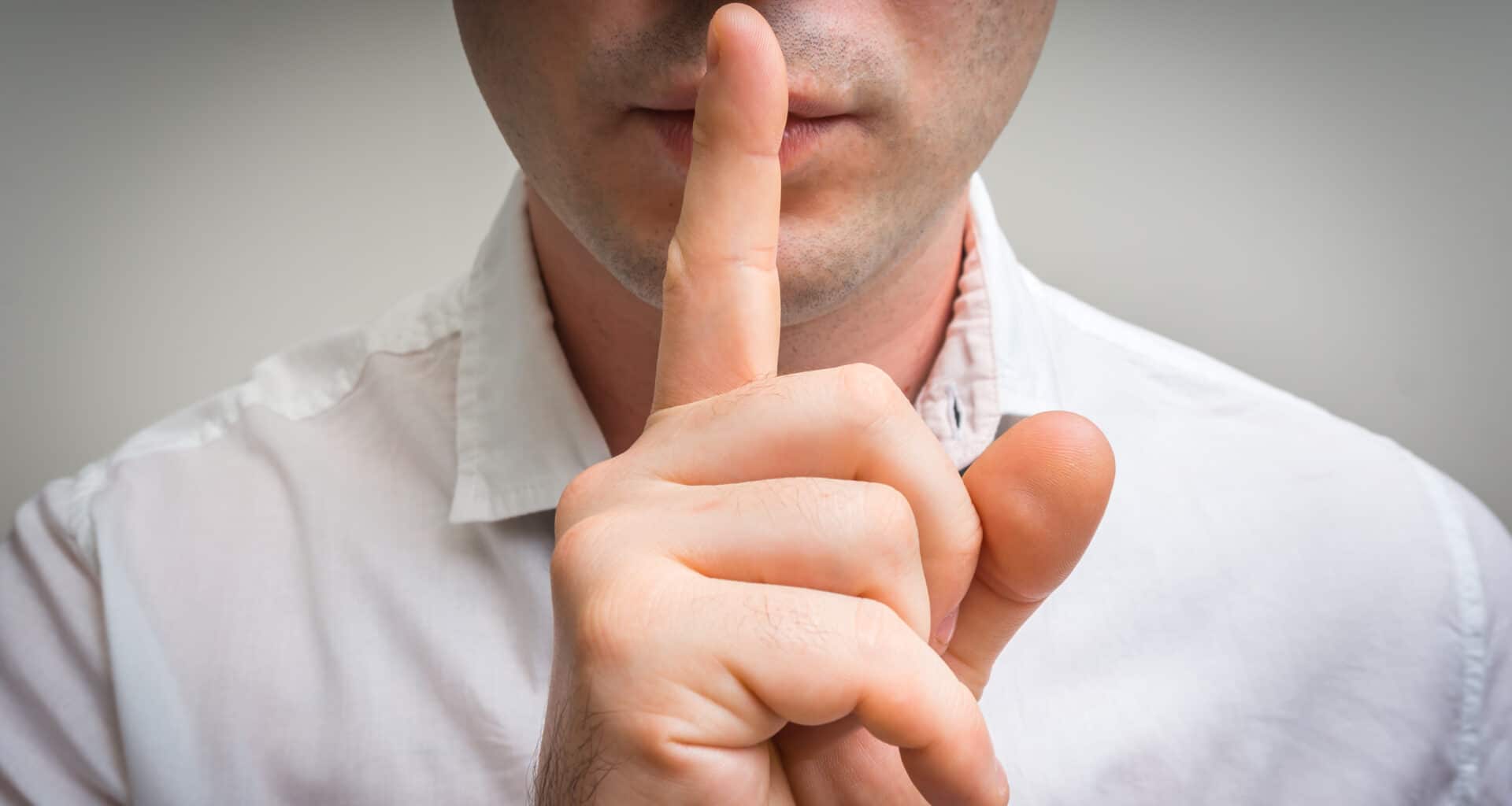 Homem colocando dedo na boca pedindo silêncio