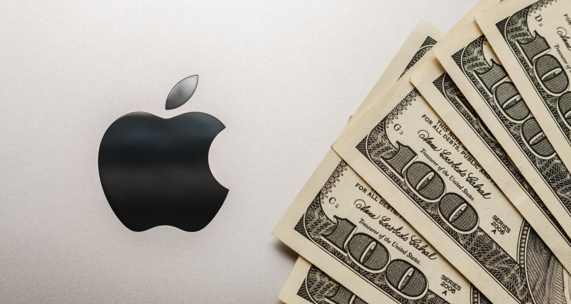 Logo da Apple em um MacBook com notas de dólares ao lado