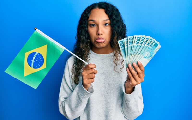 Mulher triste segurando uma bandeira do Brasil e dinheiro