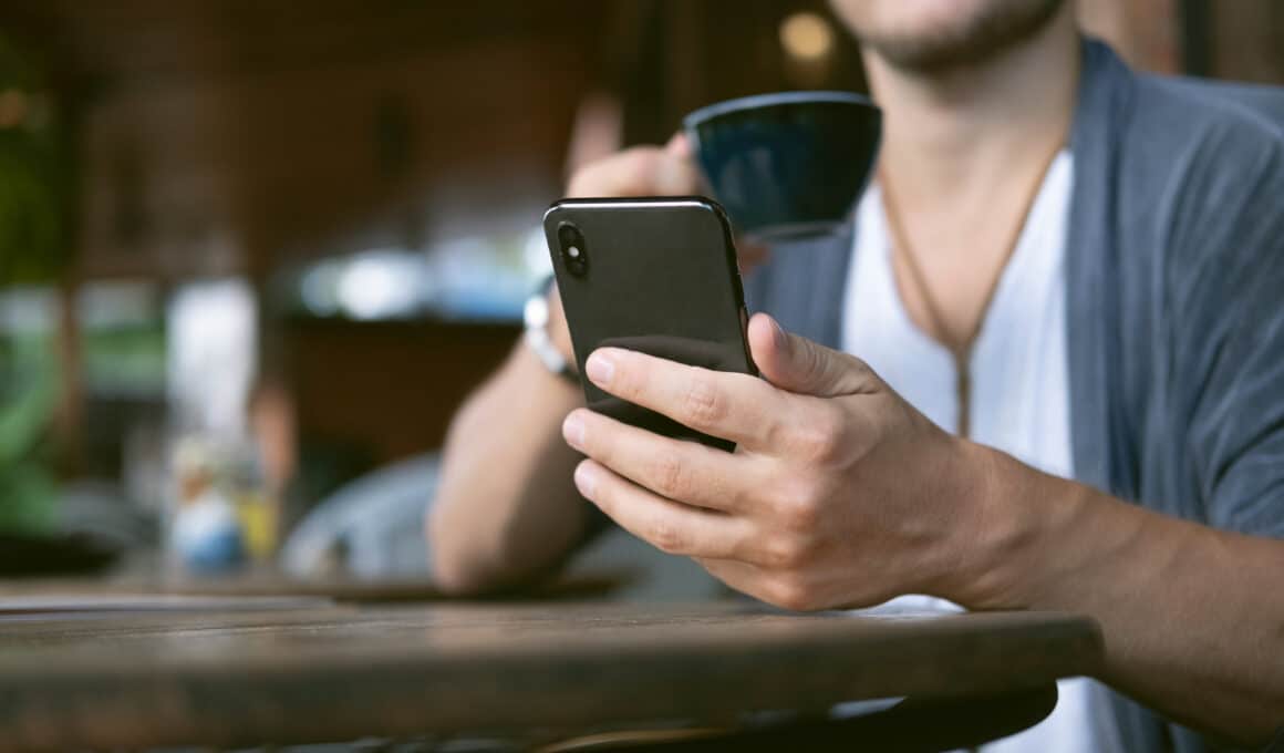 Homem tomando café e olhando para iPhone