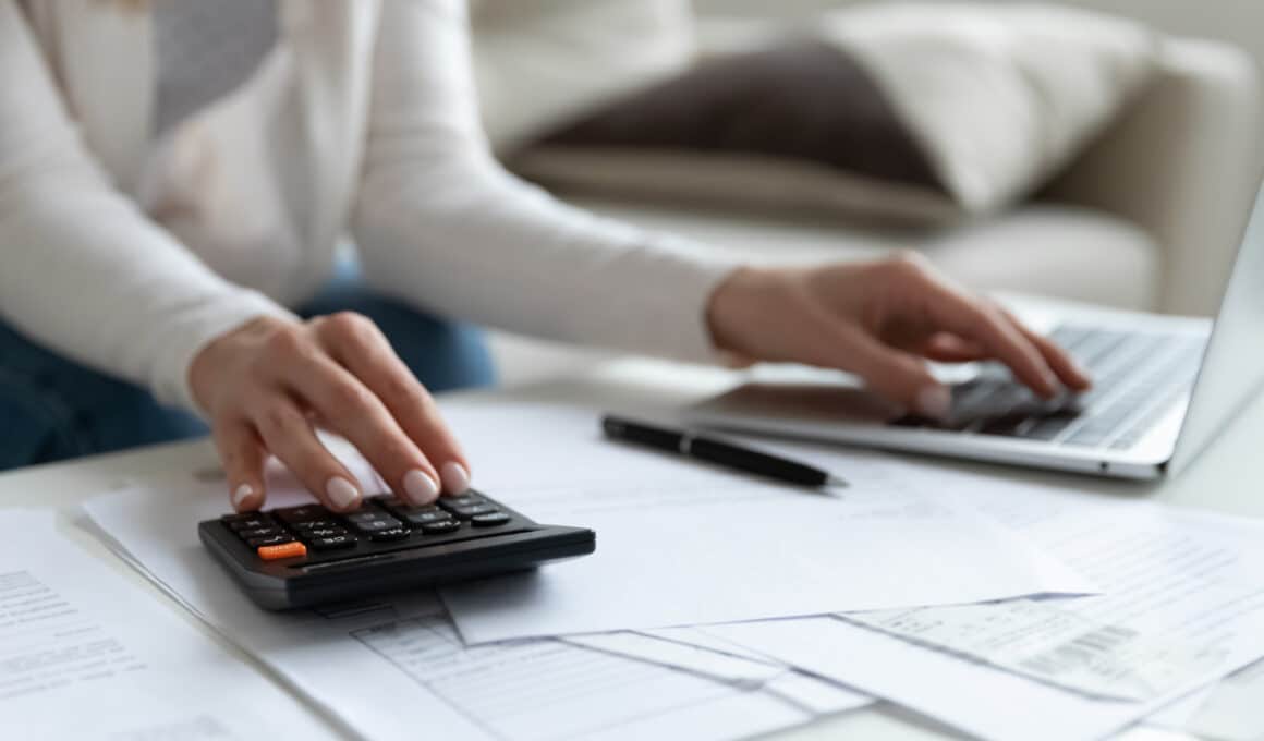 Mulher fazendo cálculos com uma calculadora e um MacBook Air (impostos)