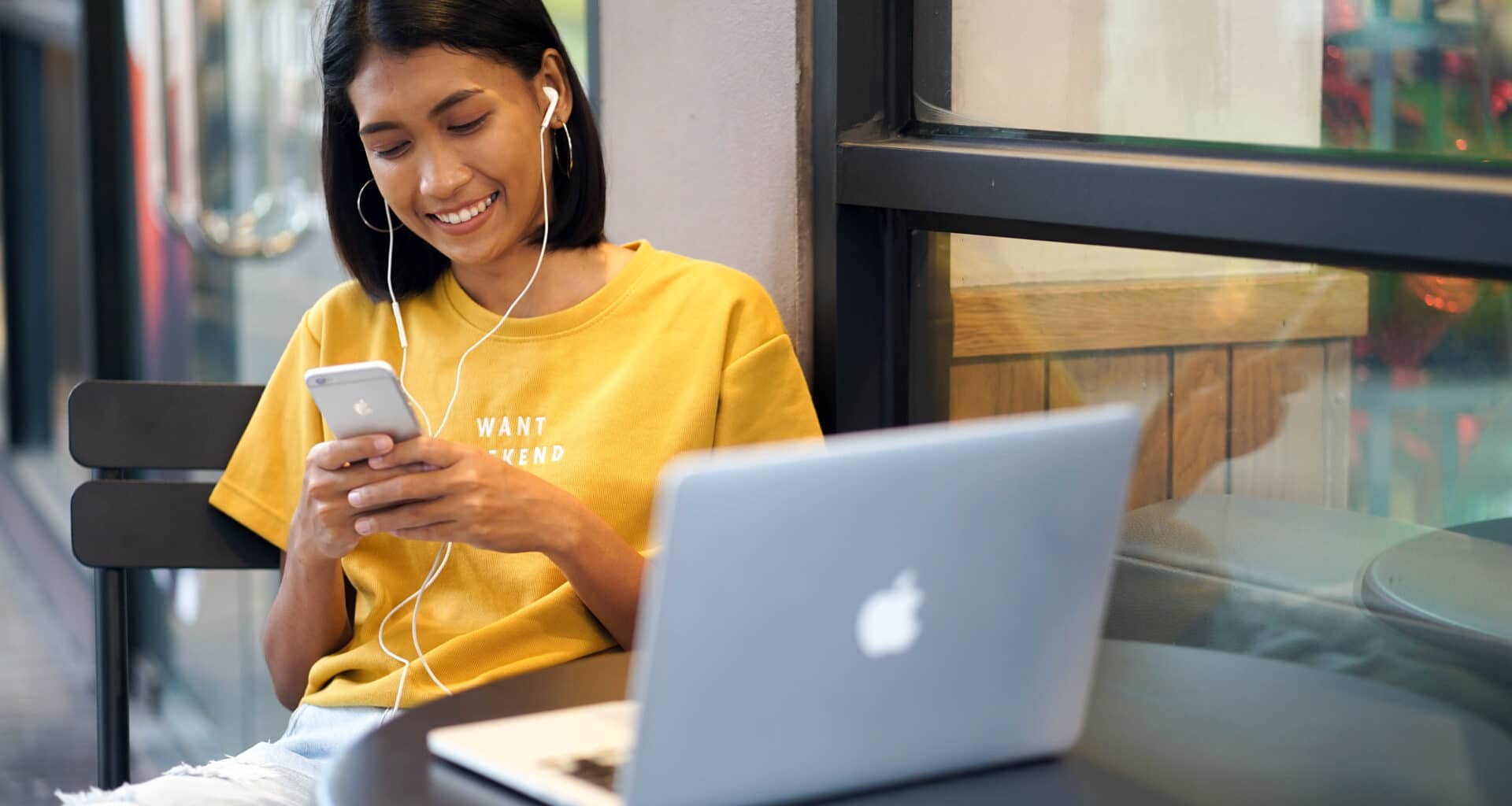 Garota lendo/usando iPhone com MacBook Air ao lado