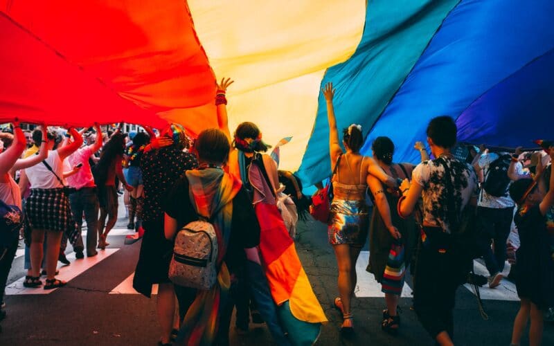 Pessoas embaixo de uma bandeira do arco-íris (LGBTQ+)
