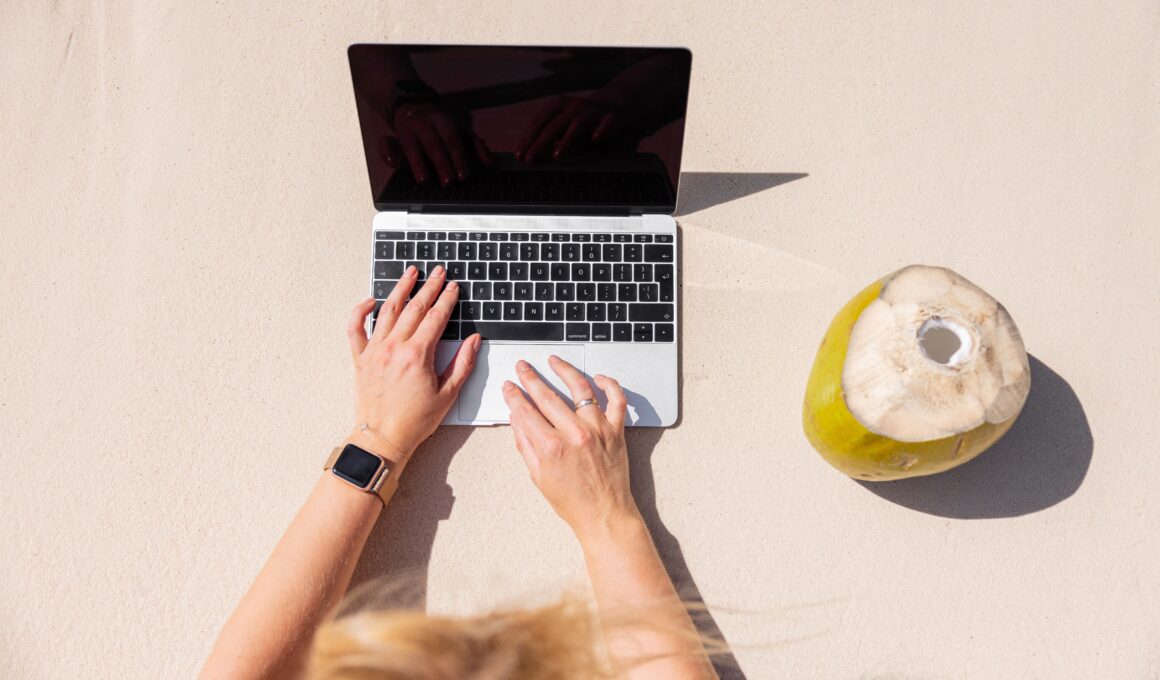 Mulher trabalhando em MacBook numa praia com côco ao lado