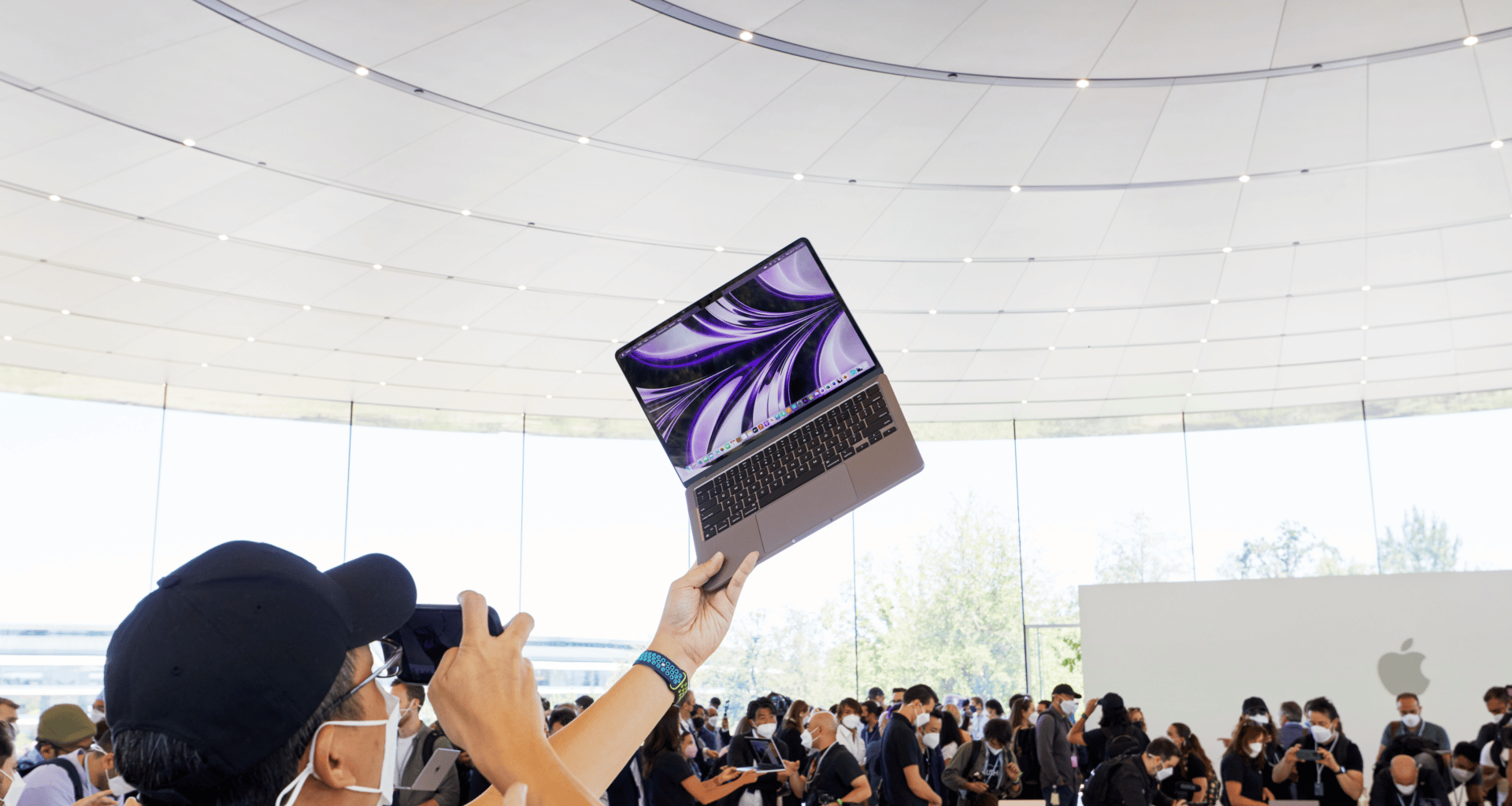 Pessoa segurando o MacBook Air M2 no ar dentro do Steve Jobs Theater do Apple Park, na WWDC22