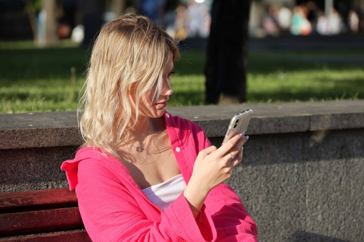 Menina usando iPhone no banco da praça