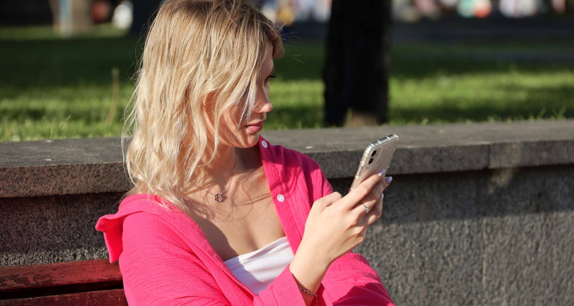 Menina usando iPhone no banco da praça