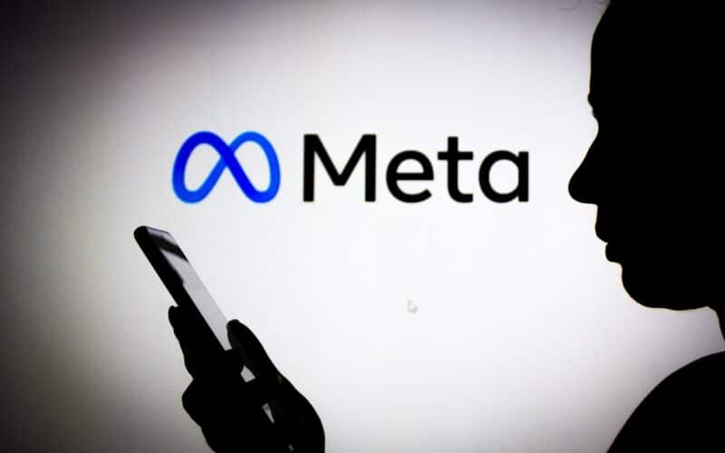 Pessoa usando celular com o logo da Meta no fundo
