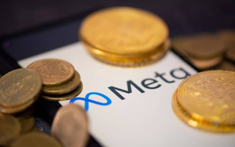 Logo da Meta em smartphone com moedas/dinheiro