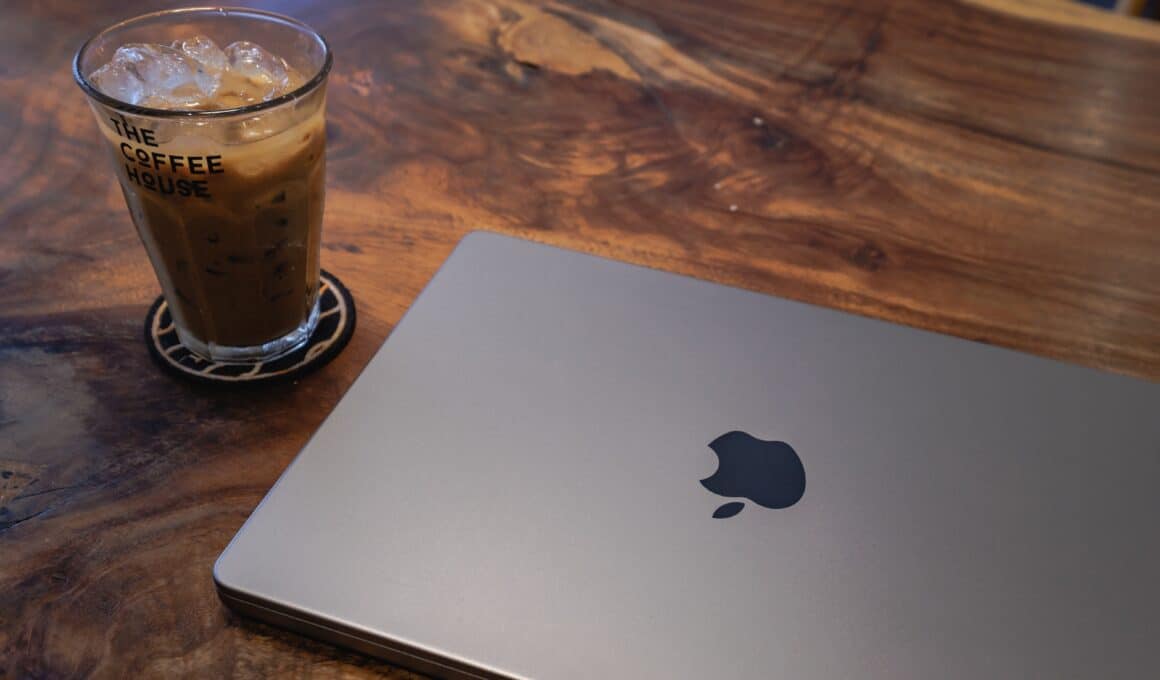 MacBook Pro de 14 polegadas ao lado de um copo com café numa mesa de madeira
