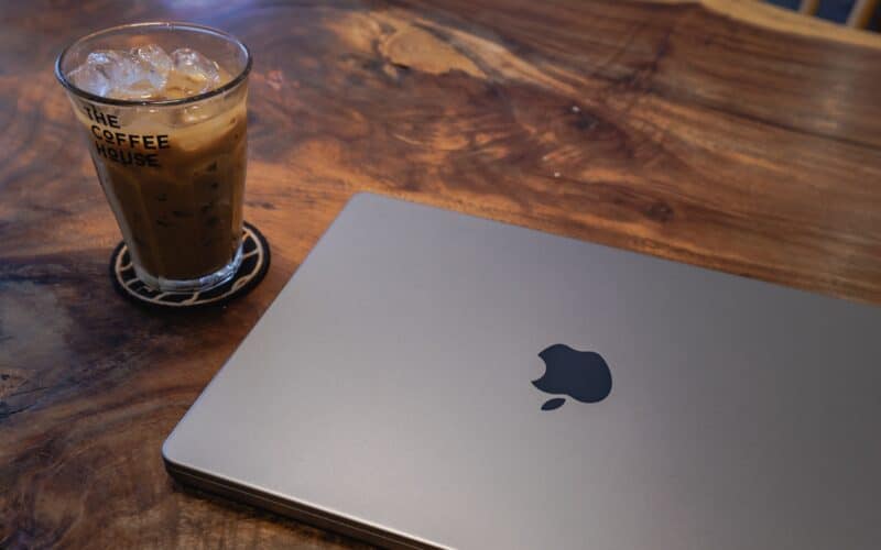 MacBook Pro de 14 polegadas ao lado de um copo com café numa mesa de madeira