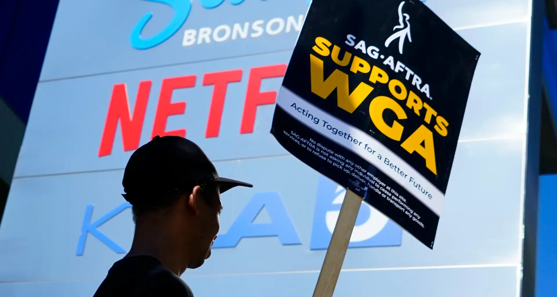 Homem segura cartaz em apoio às greves dos sindicatos dos atores e dos roteiristas de Hollywood