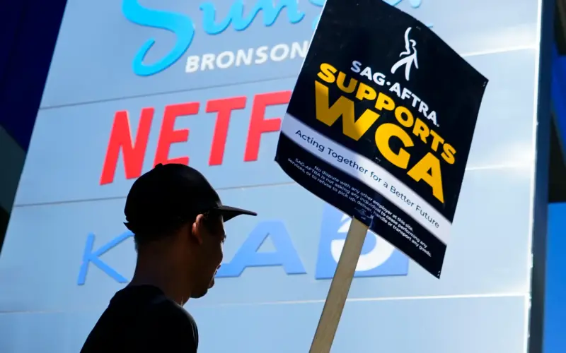 Homem segura cartaz em apoio às greves dos sindicatos dos atores e dos roteiristas de Hollywood
