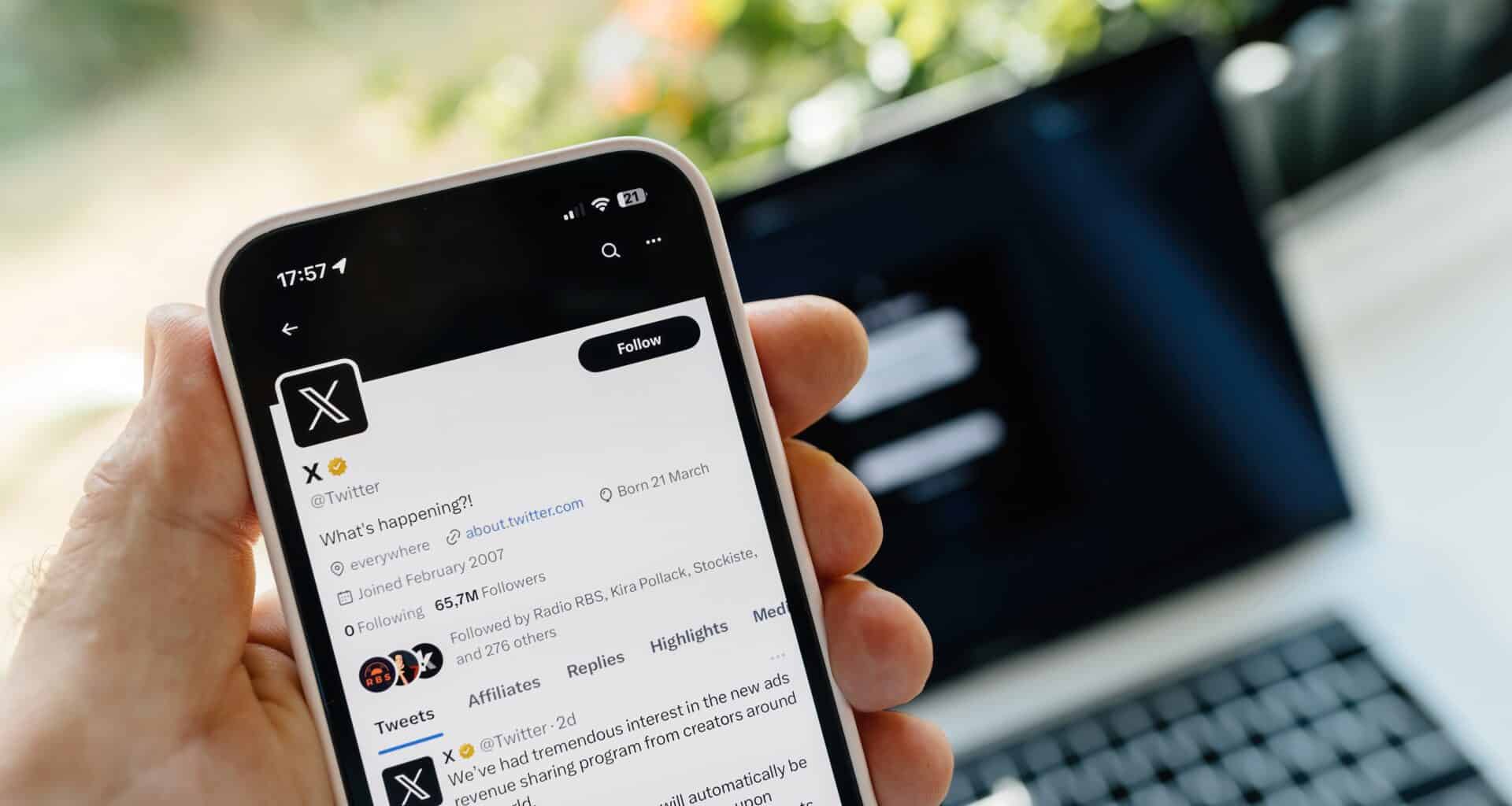 Conta do X no iPhone com um Mac ao fundo