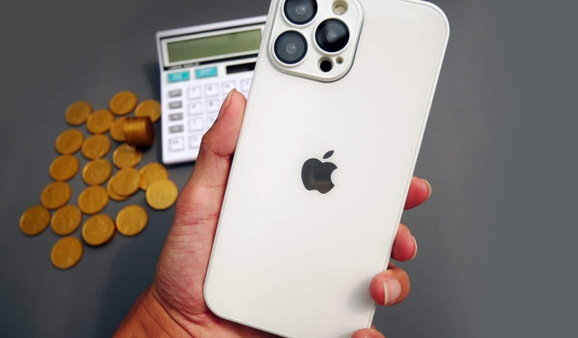 iPhone Pro Max em mão com moedas e calculadora ao fundo