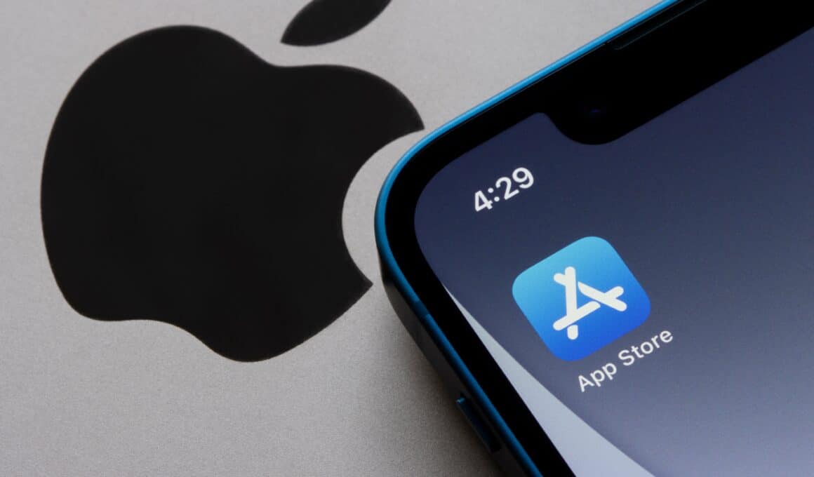 Ícone da App Store no iPhone ao lado do logo da Apple em um MacBook