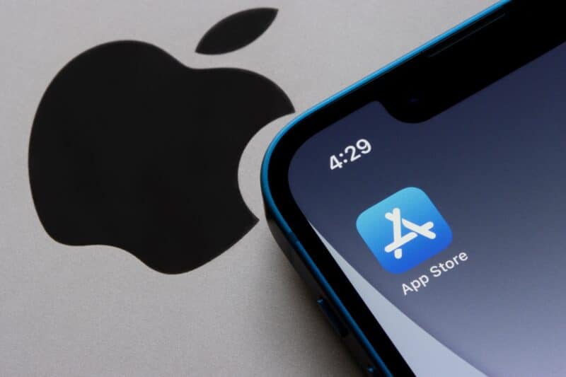 Ícone da App Store no iPhone ao lado do logo da Apple em um MacBook