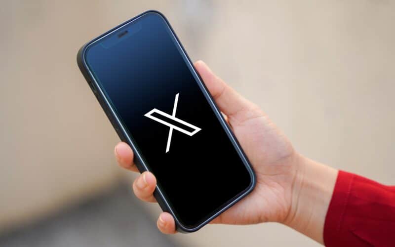 Mão segurando um iPhone com o logo do X