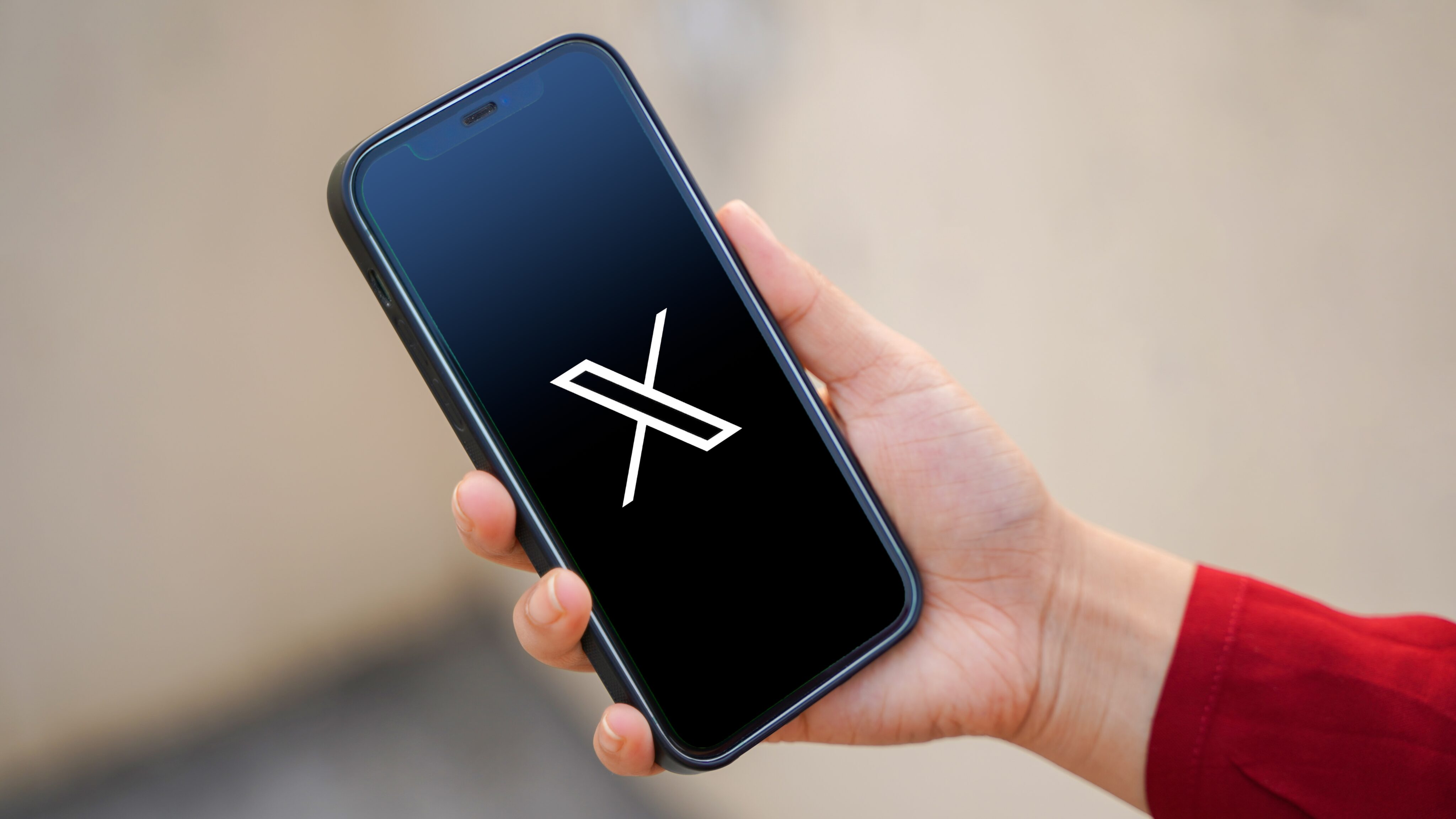 Hand holding an iPhone with the X logo