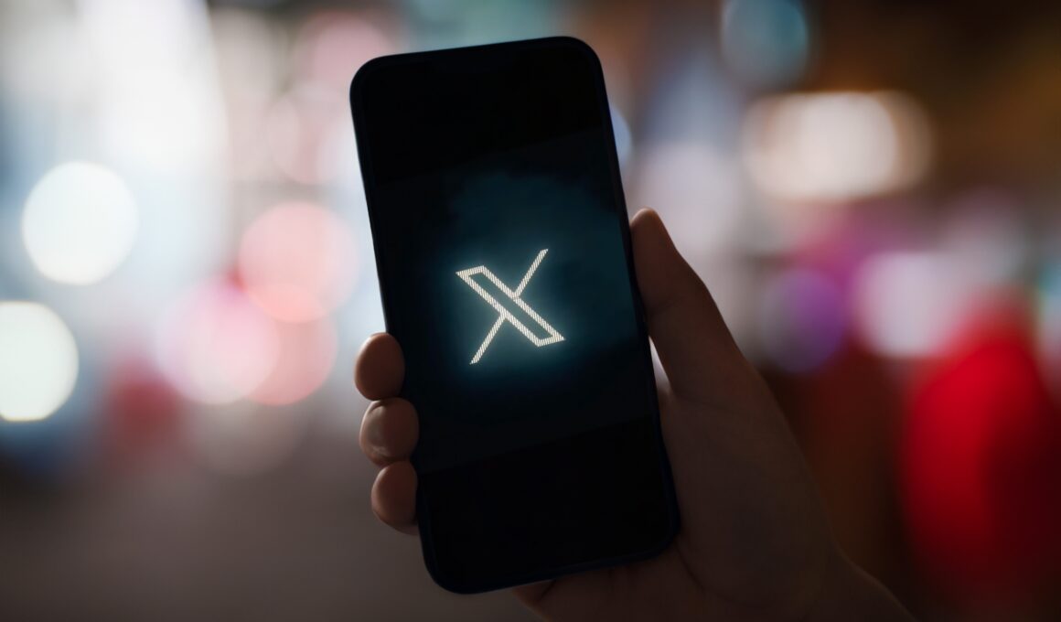 Mão segurando um smartphone com o logo do X em um fundo desfocado
