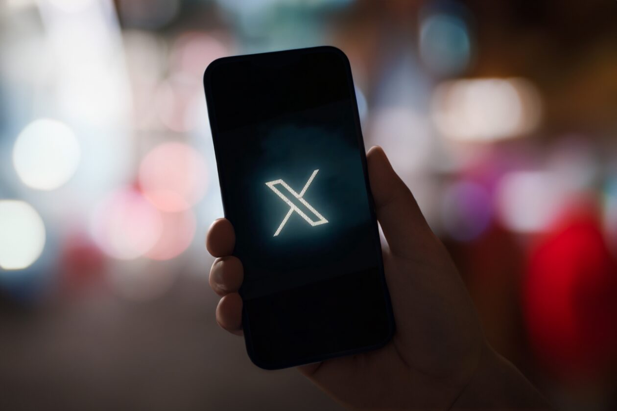 Mão segurando um smartphone com o logo do X em um fundo desfocado