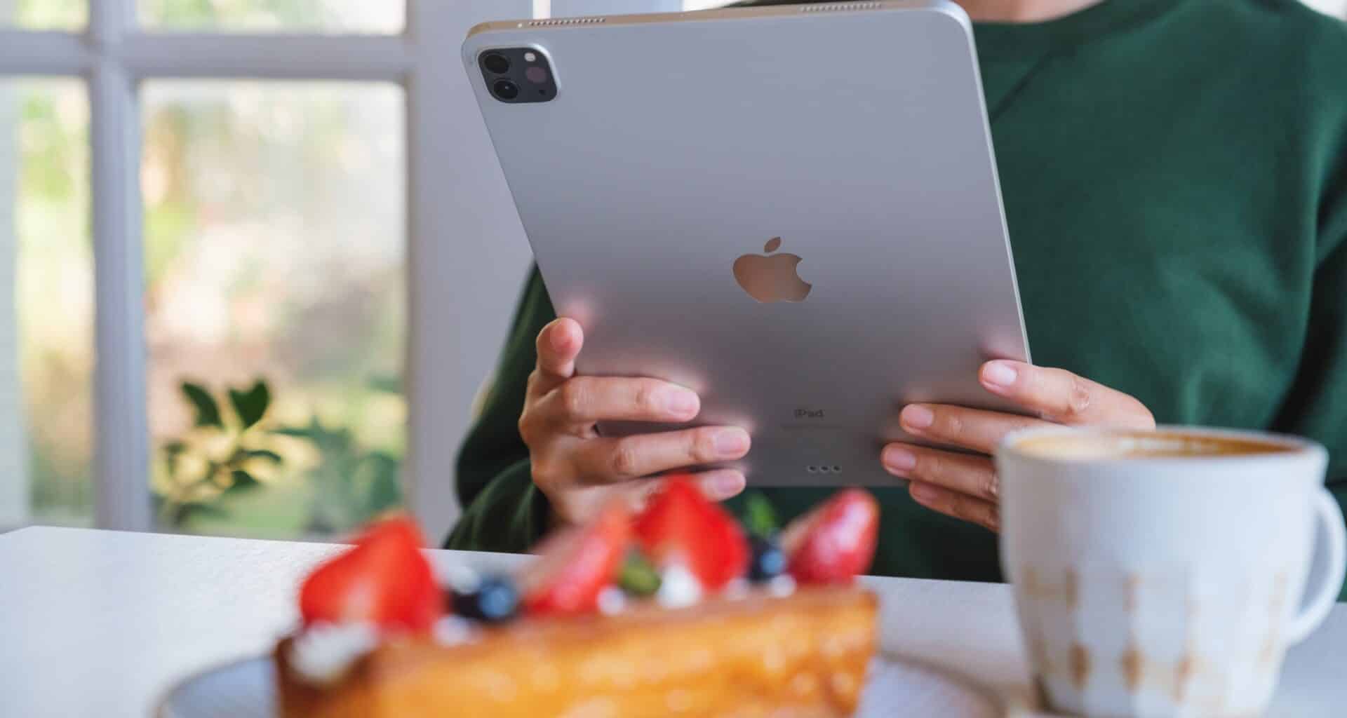 Mulher usando iPad Pro em frente a uma mesa com café e doce