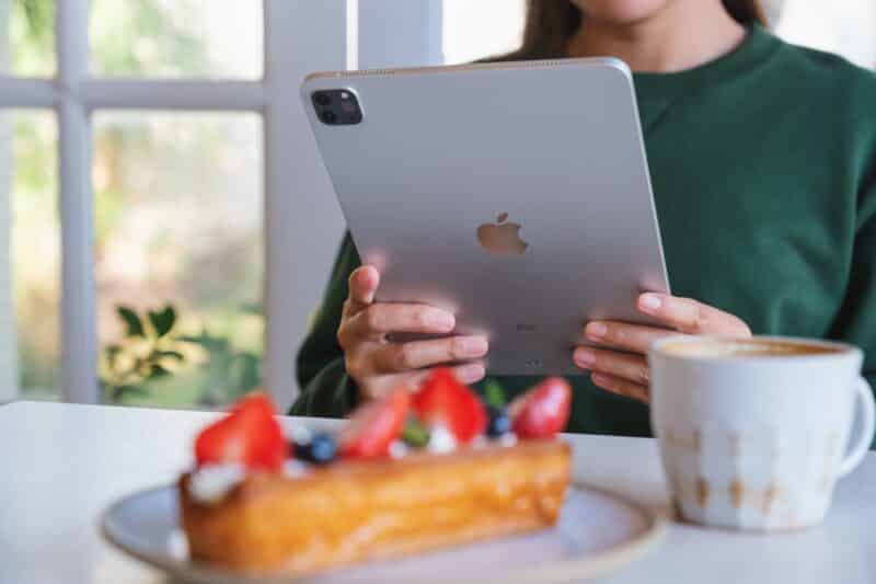 Mulher usando iPad Pro em frente a uma mesa com café e doce