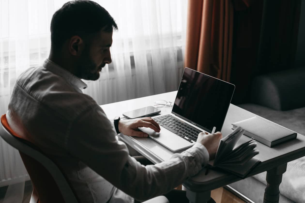 Homem usando um MacBook Pro com iPhone ao lado e fazendo anotações