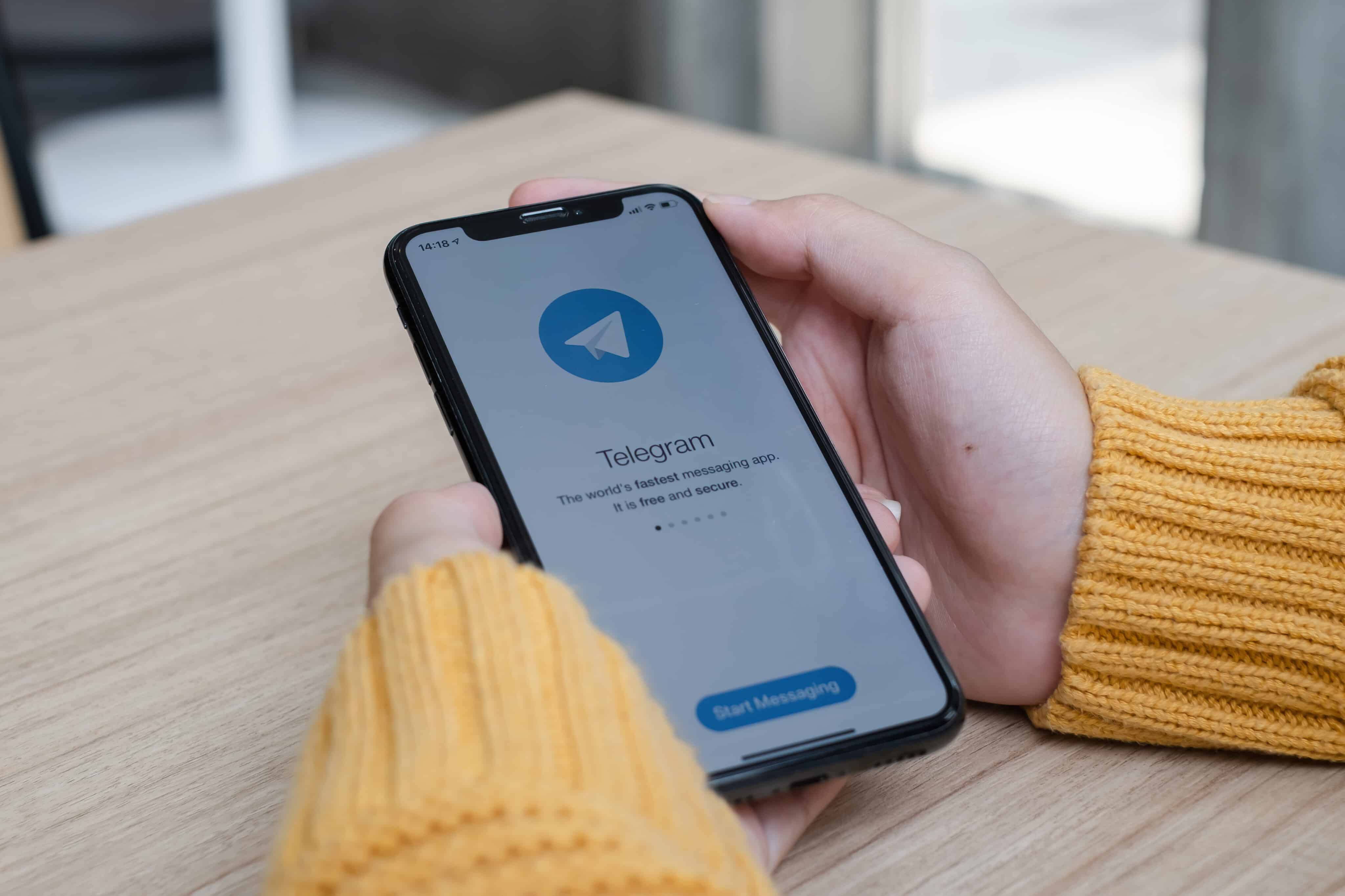 Mão segurando iPhone com o app Telegram abrindo