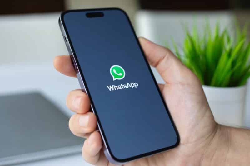 Mão segurando iPhone com o app WhatsApp abrindo