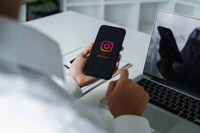 Homem segurando um iPhone rodando o Instagram com um Mac ao fundo