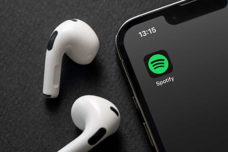 Ícone do app do Spotify na tela do iPhone com AirPods ao lado