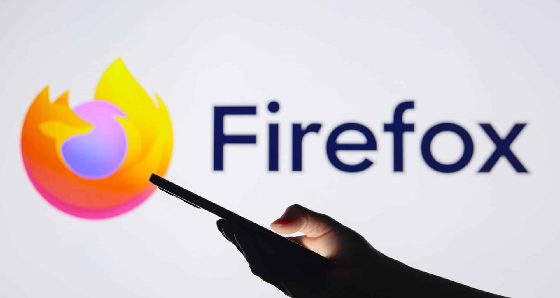 Mão segurando um telefone com a marca Firefox ao fundo