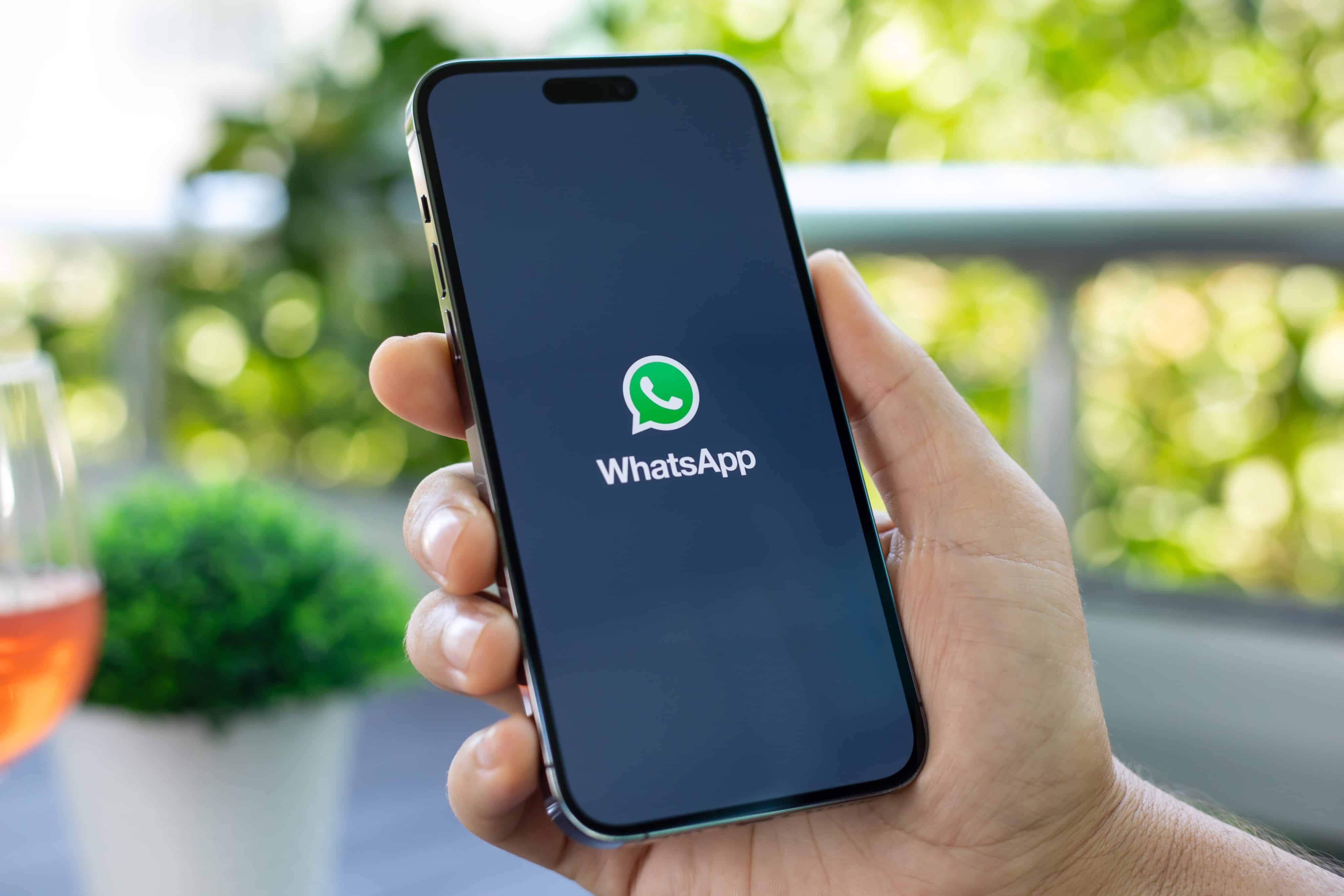 Mão segurando um iPhone 15 Pro Max com o WhatsApp