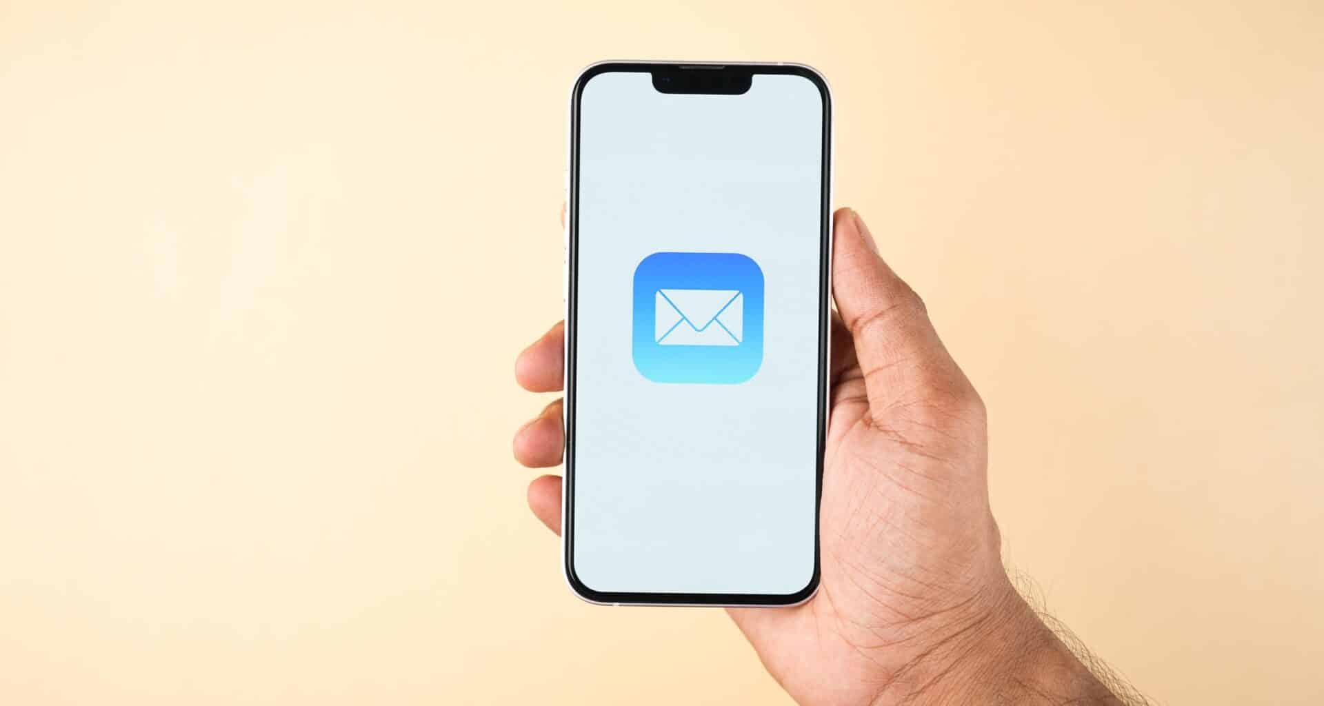 Mão segurando um iPhone com o ícone do app Mail