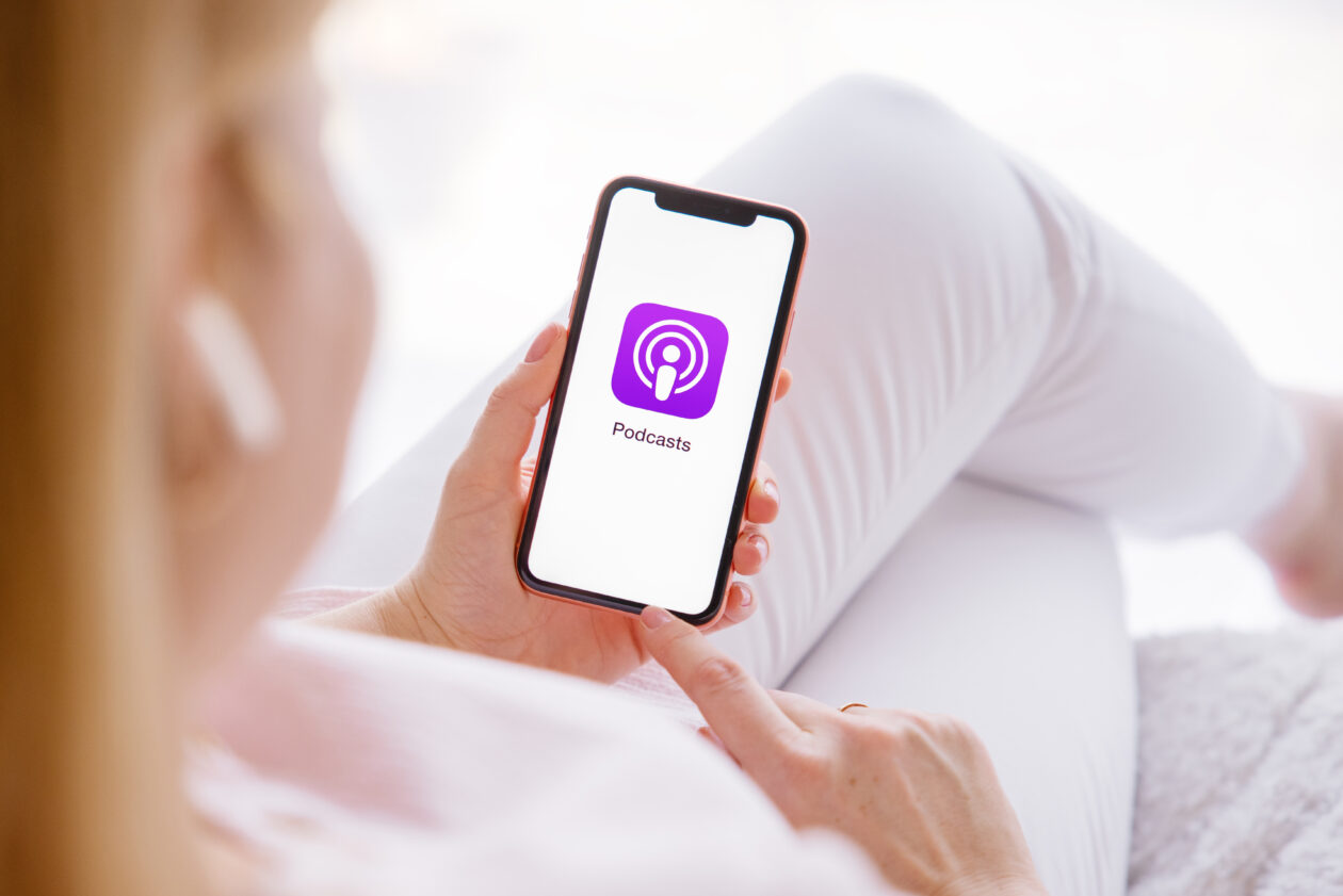 Ícone do app Podcasts na tela do iPhone segurado por uma mulher