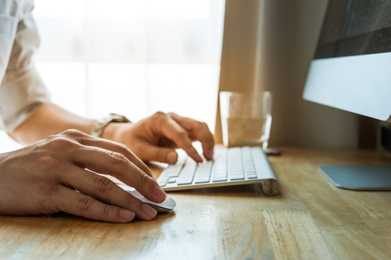 Homem digitando em antigo teclado da Apple com iMac na frente