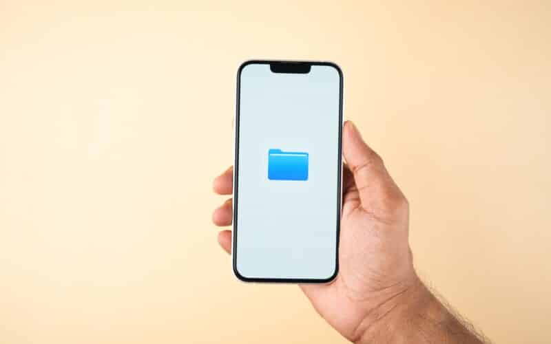Mão segurando um iPhone com o ícone do app Arquivos (Files)
