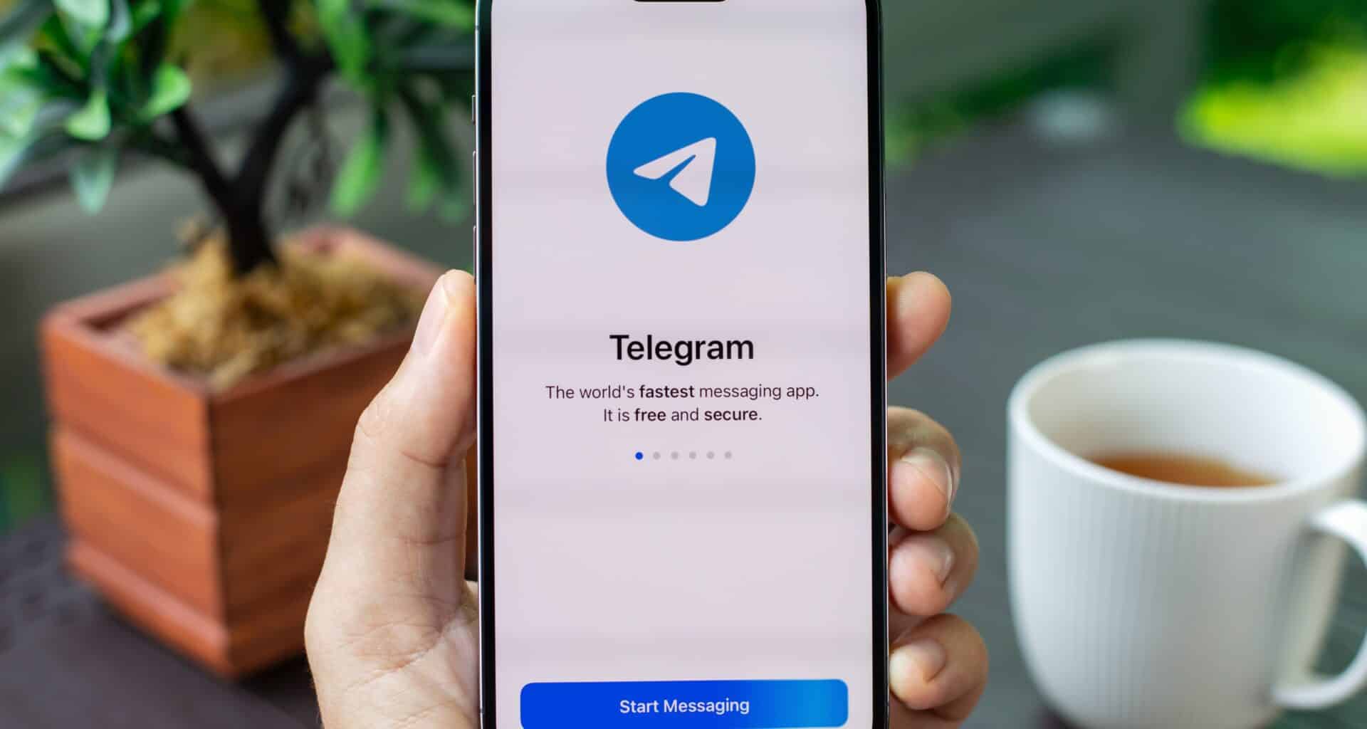 Homem segurando um iPhone 15 Pro Max com o Telegram na tela