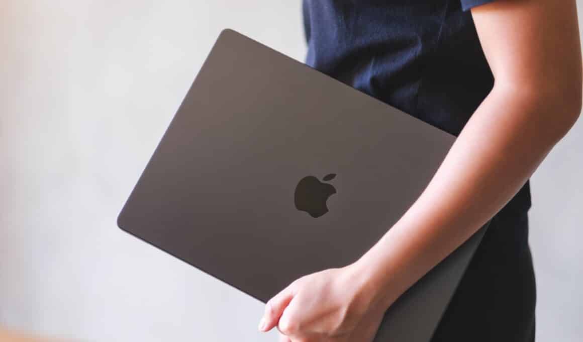 Mulher carregando um MacBook fechado no braço