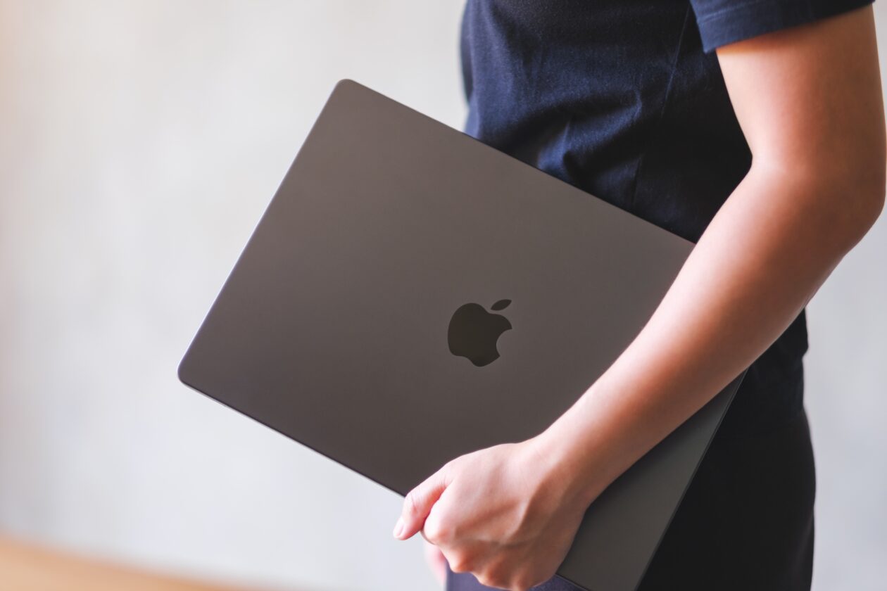 Mulher carregando um MacBook fechado no braço