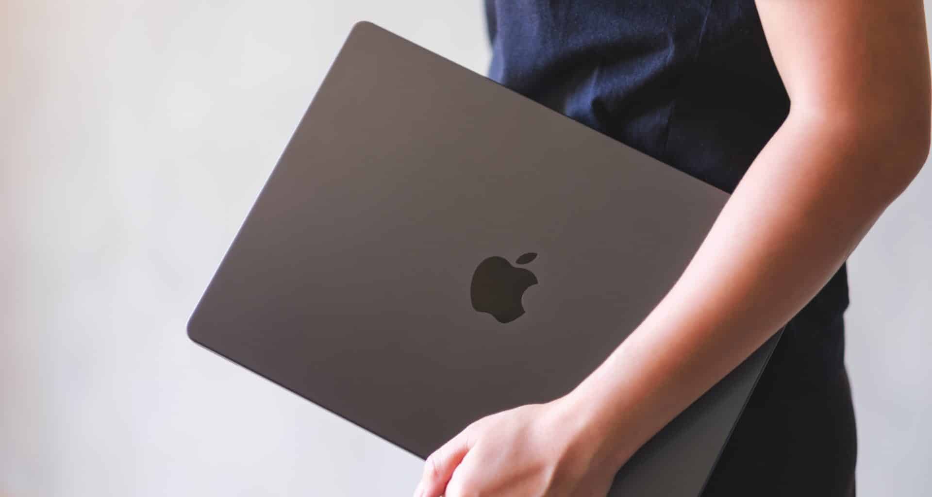 Mulher carregando um MacBook fechado no braço