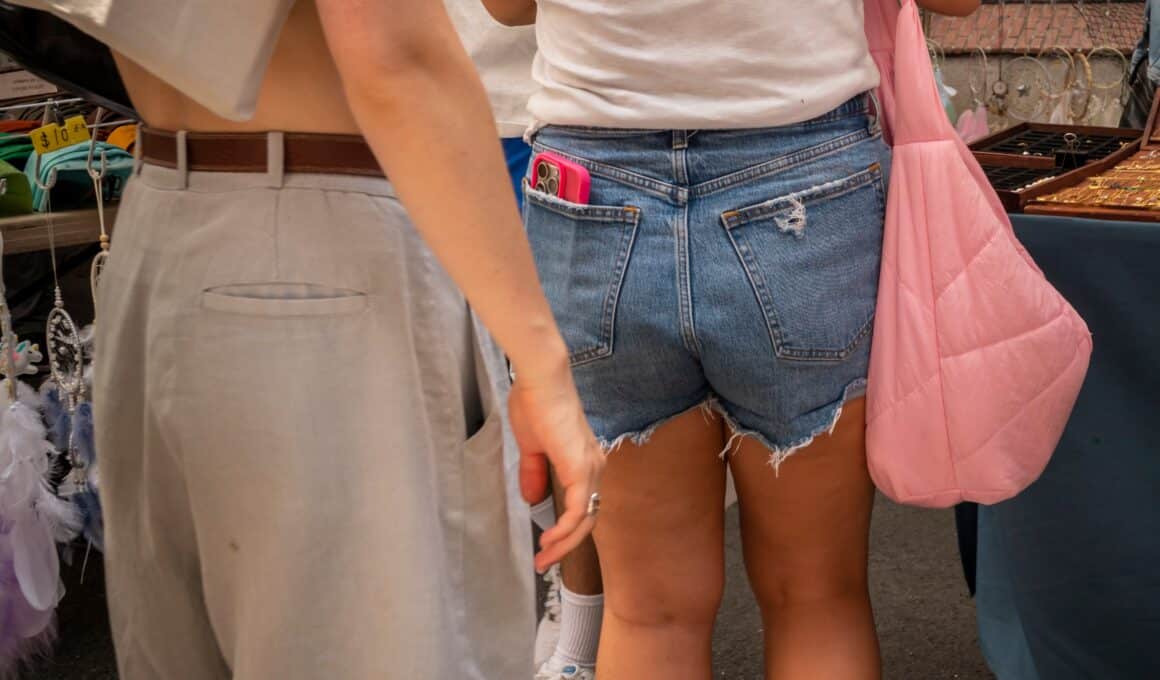 Mulher com o iPhone no bolso da calça com uma pessoa propensa a roubar o aparelho