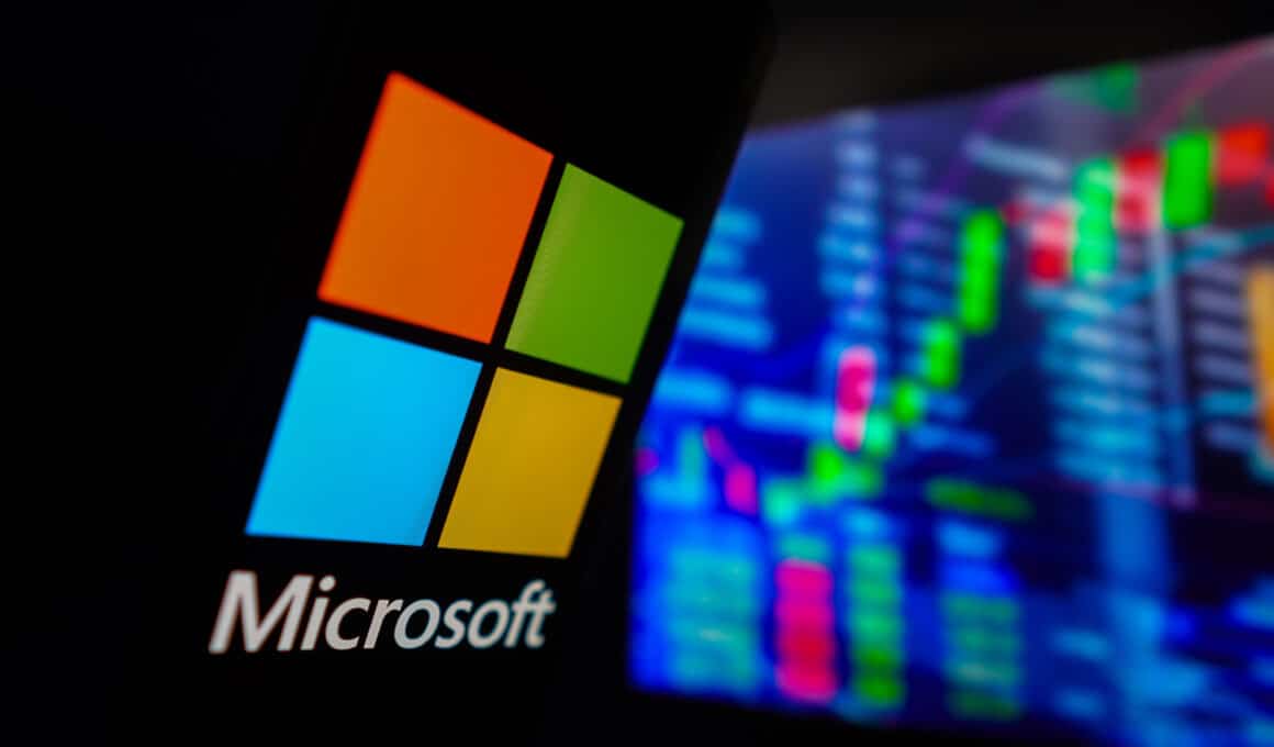 Logo da Microsoft em frente a painel com bolsa de valores