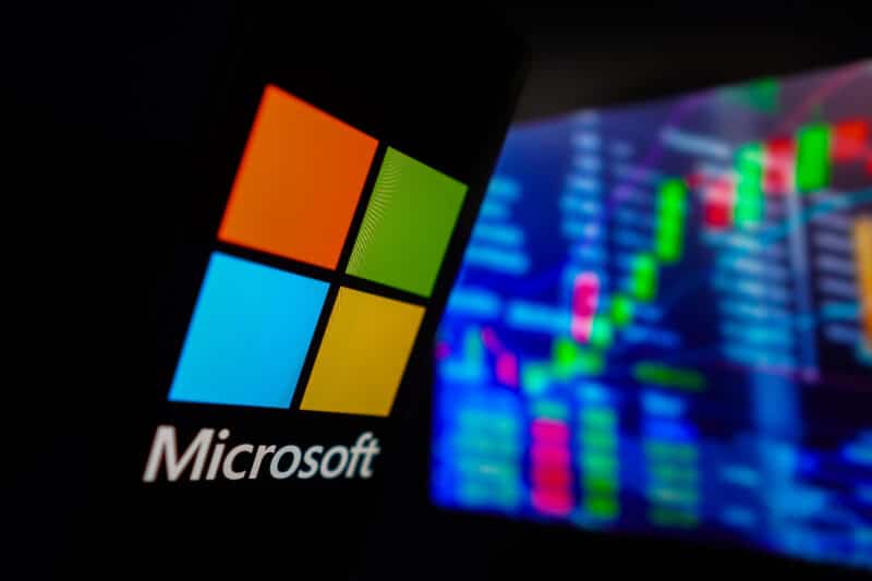 Logo da Microsoft em frente a painel com bolsa de valores